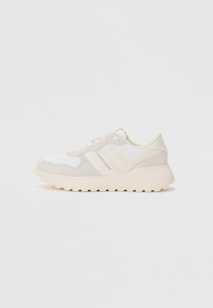 Sneakers in white and light beige with a mix of smooth and textured fabric. Features a cushioned sole and a logo accent on the side.