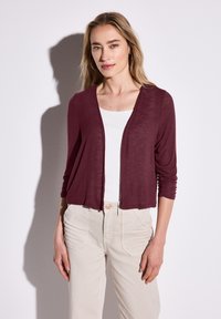 Burgundy lättviktscardigan med draperad front och trekvartärmar, lagd över en vit topp, parat med beiga byxor.