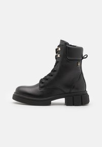 Botte de cheville en cuir noir avec un bout arrondi, lacets à l'avant, accents en métal doré et une semelle en caoutchouc épaisse.