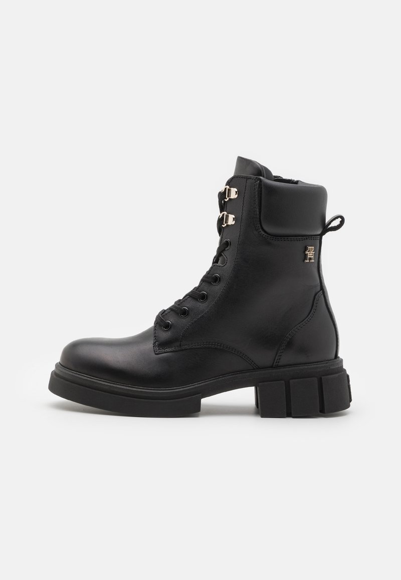 Botte de cheville en cuir noir avec un bout arrondi, lacets à l'avant, accents en métal doré et une semelle en caoutchouc épaisse.