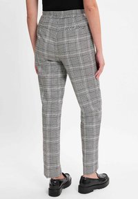 Karierte Hosen in Schwarz und Weiß mit slim Fit, strukturiertem Stoff, mittelhoher Taille und zwei Gesäßtaschen. Kombiniert mit schwarzen Schuhen.