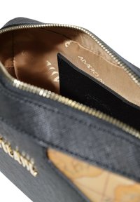 Borsa nera con cerniera realizzata in materiale testurizzato con dettagli in metallo dorato. L'interno presenta una fodera liscia di colore marrone chiaro e uno scomparto per carte di credito nero.