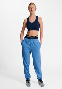 Marine sports-bh, lyseblå joggers med elastisk talje, tætsiddende ben og sort branding. Grå træningssko med snørebånd og netdetaljer.
