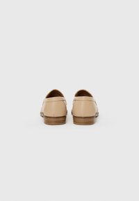 Beige Lederloafers mit einem niedrigen, gestuften Absatz, abgerundetem Rücken und leichten Nähdetails an den Nähten. Glatte Textur mit einem minimalistischen Design.