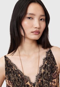 Top in raso con bordo in pizzo, caratterizzato da un motivo leopardato in tonalità di marrone e nero. Tessuto simile al satin con design a scollo a V profondo.