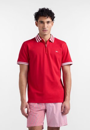 Czerwona koszulka polo z białym zamkiem przy kołnierzu i paskami na rękawach, zestawiona z czerwono-białymi spodenek z paskami. Gładka tekstura, casualowy design.