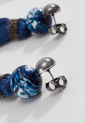 Coppia di orecchini a perno in argento con perla tonda marmorizzata blu e bianca e dettaglio con nappina blu navy su sfondo bianco.