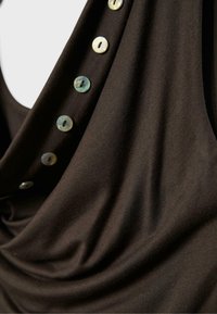 Krupan plan tamnobraon tkanine s nizom malih, okruglih, iridescentnih dugmadi duž ruba prebačene odjevne tkanine.