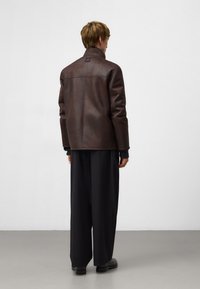 Bruine leren jas met een hoge kraag, met een gladde textuur en minimale stiksels. Draag het over zwarte wijde broeken en chunky schoenen.