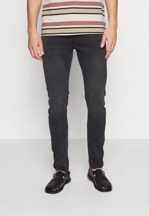 Jeans slim fit de color gris oscuro combinados con una camiseta de rayas beige y burdeos. Sandalias de tejido negro completan el conjunto.