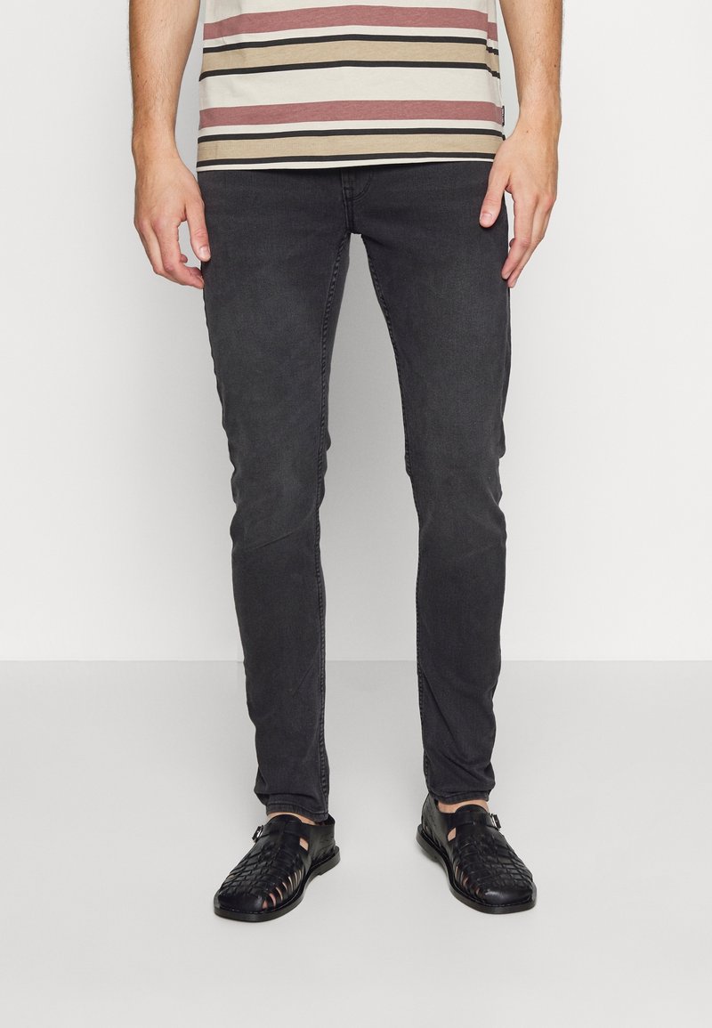 Tmavě šedé slim fit džíny spárované s béžovým a burgundským pruhovaným tričkem. Černé tkané sandály dokončují outfit.