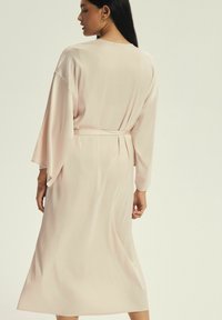 Jasnoróżowy satynowy szlafrok z paskiem, długimi rękawami i luźnym krojem. Gładka tekstura i minimalistyczny design, sięgający do połowy łydki.