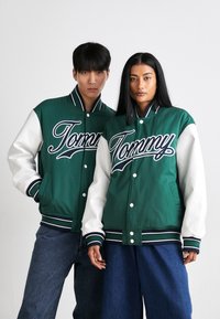 Casacos varsity verdes e brancos com um proeminente bordado "Tommy", punhos em ribana listrados e fecho de botão. Usados com denim.