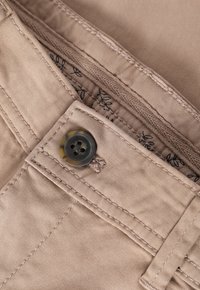 Beige Baumwollhosen mit einer subtilen Textur, ausgestattet mit einem dunkelbraunen Knopf und dekorativen Nähten entlang des Bundes und der Tasche.
