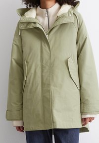 Ljusgrön parka med en mjuk fleecefoder i kragen, framdragkedja och sidofickor. Har rak passform och knäppta ärmslut.