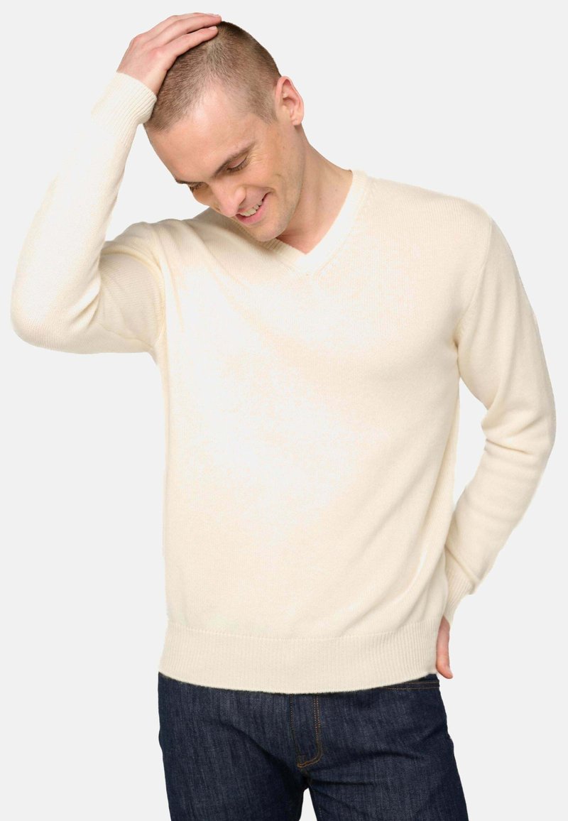Sweater crème à col en V en tissu tricoté doux, avec des poignets et un ourlet côtelés, associé à un jean bleu foncé.