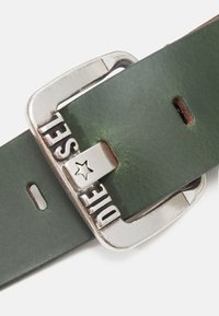 Cintura in pelle verde con fibbia in metallo argentato che presenta testo inciso e un accento a stella; texture liscia e diversi fori di regolazione.