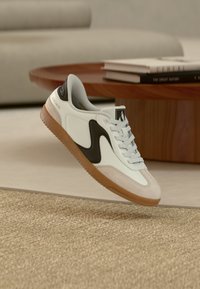 Sneaker bianco e marrone con tomaia in pelle liscia, dettagli in camoscio, logo nero e suola in gomma color gomma, con design con lacci.