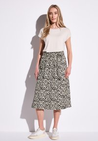 Beige midi-jurk met zwart abstract patroon, met een hoge taille en plooien. Gecombineerd met een crèmekleurig t-shirt en witte sneakers.