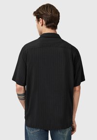 Sort kortærmet skjorte med vertikale striber og knap-ned krave. Teksturert stof med en afslappet pasform. Baghaven vist, parret med denim.