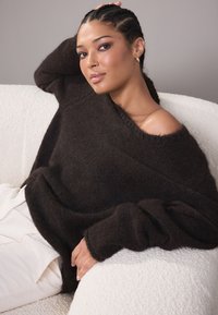 Liiga suur, tumesinine kampsun, valmistatud pehmest ja tekstuuriga materjalist, laiade varrukatega; kantud ühelt õlalt alla tõmmatud; sobitatud heledate pükstega.