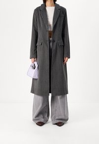 Šedý pruhovaný kabát s klopovým límcem a předními kapsami, v kombinaci se světlými šedými oversized džíny a malou levandulovou kabelkou.