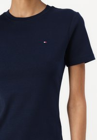 Navy cotton t-shirt with a round neckline, short sleeves, and a small red, white, and blue logo on the left chest. Soft texture.