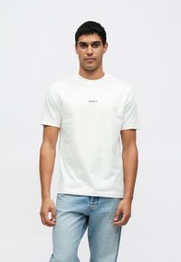 Valge lühikeste varrukatega puuvillane T-särk, mille rinnal on keskel väike must "Boys Club" logo. Standardmõõdus, ümara kaelusega disain.