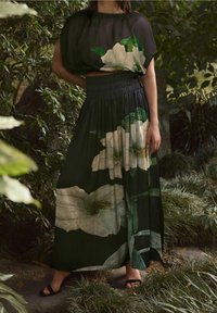 Schwarzes Blumenkleid Maxikleid mit weißen Blumenprints und grünen Blättern, ausgestattet mit einem gerafften Taillenbund und einem fließenden, strukturierten Stoff.