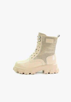 Beżowe botki za kostkę o błyszczącej powierzchni, z siateczkowym panelem bocznym, metalowymi akcentami, okrągłym noskiem i masywną gumową podeszwą. Posiadają klasyczne sznurowanie.
