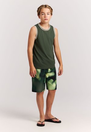 Chemise sans manches verte avec bordure blanche, associée à un short de bain vert tie-dye. Des tongs noires complètent la tenue.