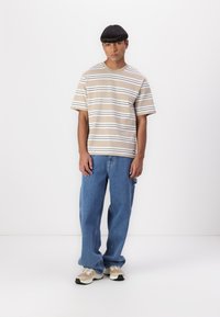 Striped beige and white t-shirt, loose blue jeans, and beige sneakers with accents. Casual fit, mid-length sleeves, and relaxed style.
