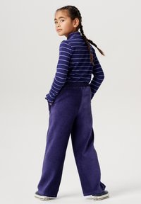 Lila ribbad kordfläckbyxor med avslappnad passform, kombinerade med en långärmad marinblå randig topp. Har en hög halsringning och detaljer på baksidan.