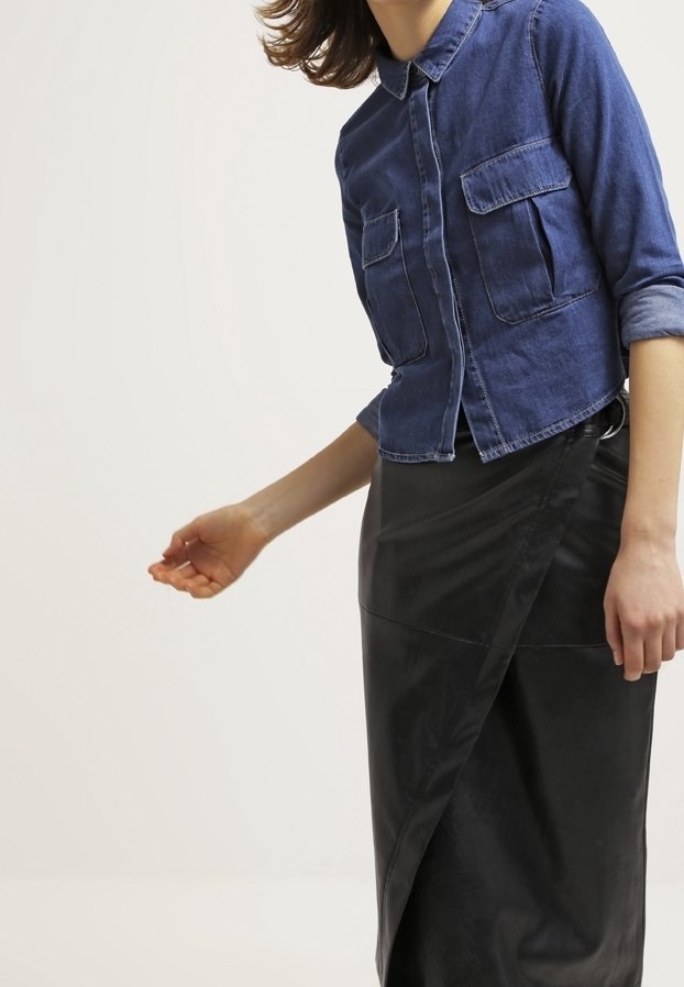 Chemise en denim bleu foncé avec deux poches poitrine, fermeture boutonnée à l'avant et manches retroussées. Jupe portefeuille en similicuir noir avec un design diagonal.
