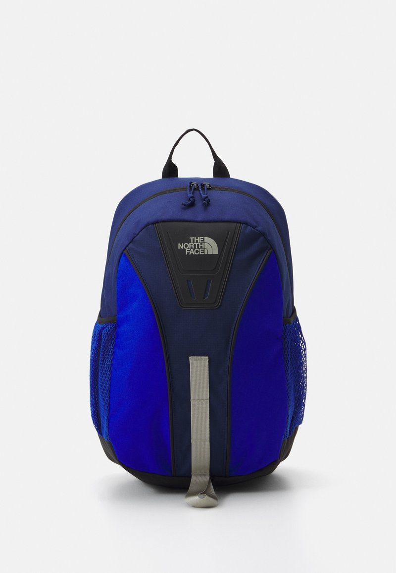 Sac à dos North Face bleu et noir avec double fermeture éclair sur le dessus, sangle réfléchissante à l’avant et poches latérales en mesh, positionné debout sur fond blanc.