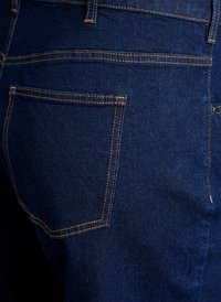 Tumedate sinine denimist teksad, millel on tagatasku kollaste tikanditega, tekstuuriga viimistlus ja klassikaline viie-tasku disain.