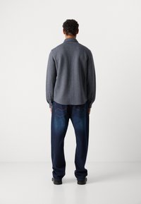 Dark navy button-up shirt with herringbone texture, paired with loose-fitting dark denim jeans featuring contrasting stitching and back pockets.