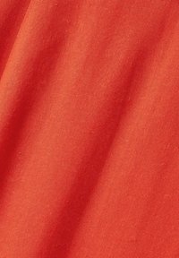 Tissu en coton rouge avec une texture lisse, légèrement froissé, montrant des variations subtiles de teintes et une couleur unie sans motifs ni accents.