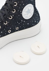 Högaxlade svart och vit kanvaskängor med ett prickigt mönster, utrustade med silverögon och vita snören bredvid.