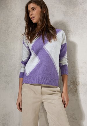 Pull en maille violet et gris avec un design géométrique, un col rond et des poignets côtelés. Associé à un pantalon beige, sur un fond neutre.