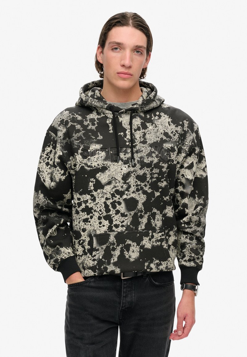 Czarna bluza z kapturem w szarym nakrapianym wzorze, ze sznurkiem do regulacji w kapturze i przednią kieszenią. Tkanina ma miękką teksturę i luźny krój.