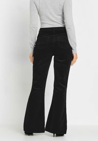 Zwarte fluwelen flare broek met een hoge taille, voorzien van twee achterzakken en een zachte textuur, gecombineerd met een lichtgrijze lange mouw top.