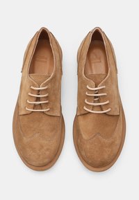 Scarpe da uomo in camoscio tan con design a wingtip, punta rotonda e lacci beige. Presentano cuciture visibili e una fodera interna in pelle liscia.