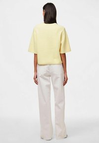 Żółty sweter z krótkim rękawem o teksturowanej powierzchni zestawiony z jasnoszarymi spodniami typu wide-leg, widok z tyłu.