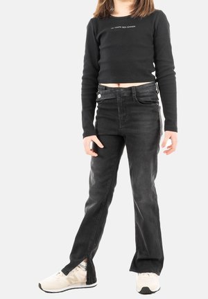 Czarny prążkowany krótki top z długim rękawem z logo, zestawiony z czarnymi, wysokim stanem jeansami o rozszerzanych nogawkach i bocznych rozcięciach. Białe trampki.