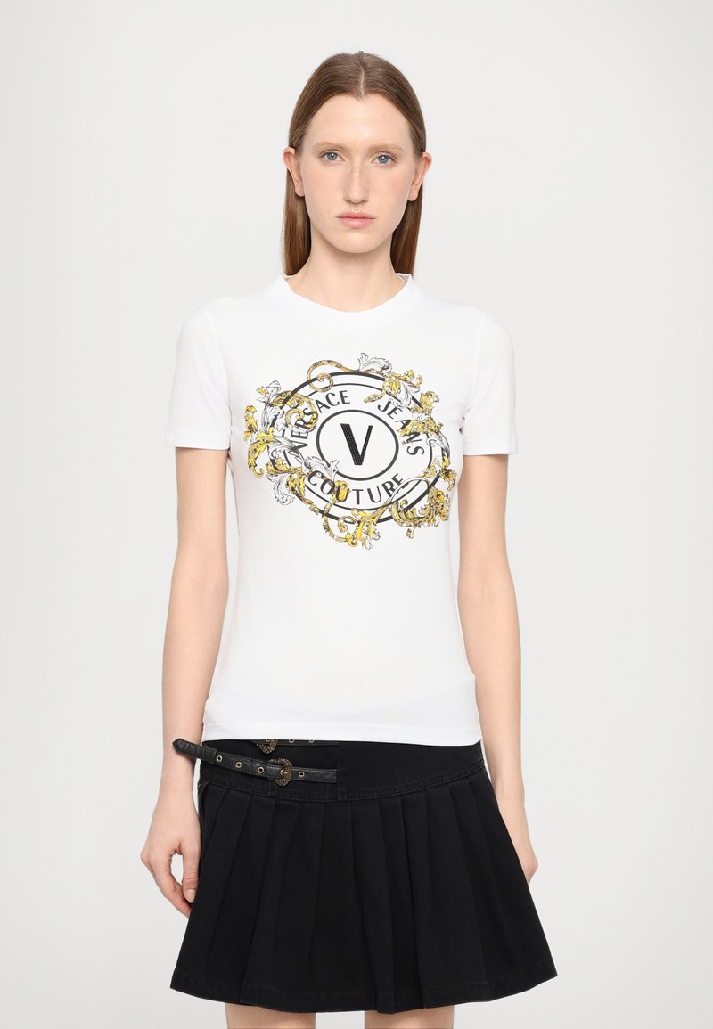 Valge puuvillane T-särk, mille esiküljel on must ja kuldne graafika "Versace Jeans Couture" ning dekoratiivsed barokkielemendid. Must volangseelik.