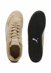 Μπεζ σουέντ αθλητικά παπούτσια με λευκές λεπτομέρειες, με στρογγυλεμένη μύτη, κορδόνια και μαύρη λάστιχη σόλα με υφασμένο σχέδιο. Ορατό το λογότυπο Puma.