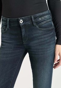 Jeans de mezclilla azul oscuro con un diseño clásico de cinco bolsillos, cierre de botón y una sutil textura desvaída a lo largo de las piernas.