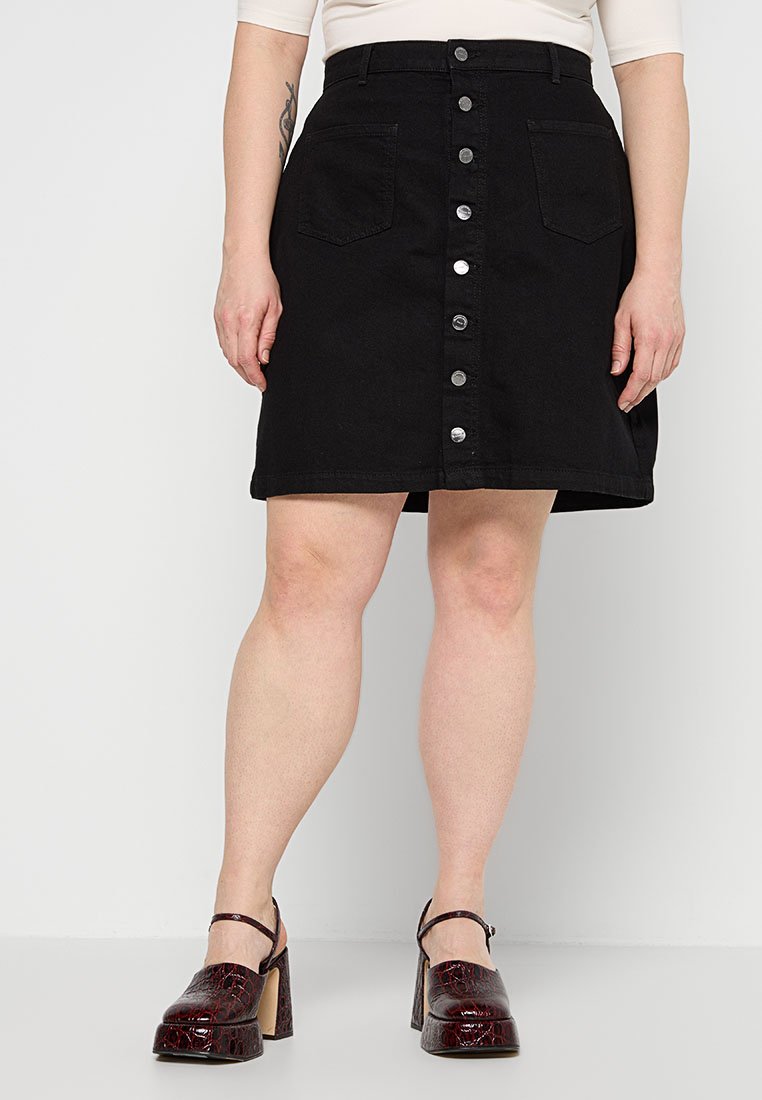 Schwarzer Denim-A-Linie-Rock mit vorderen Knöpfen, Seitentaschen und einem rohen Saum. Getragen mit bordeauxfarbenen High Heels.