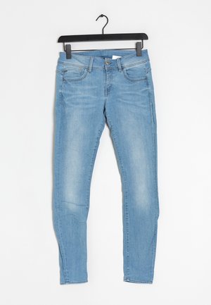 Jean slim fit bleu clair avec poches avant suspendu sur un cintre en plastique noir sur fond blanc.